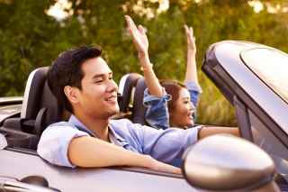 Smiling man and woman driving convertible car