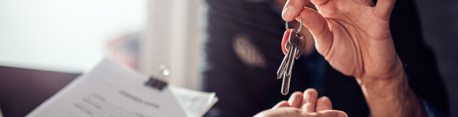 Real estate agent sitting at the desk by the window and passing keys to his client in the office