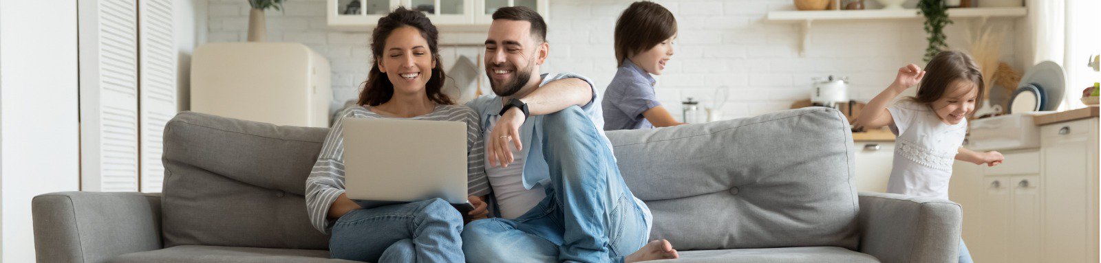 Couple on couch using computer while kids run past
