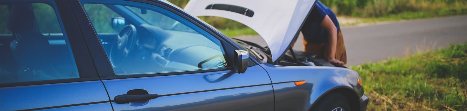 Man looking into the engine of broken down car