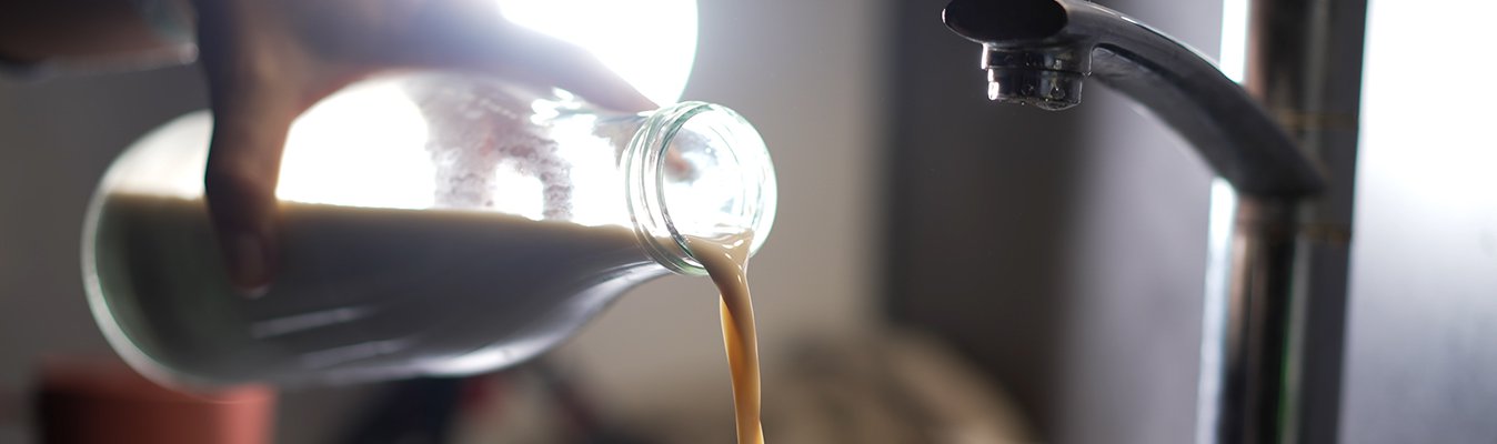 Hand pouring milk down a sink