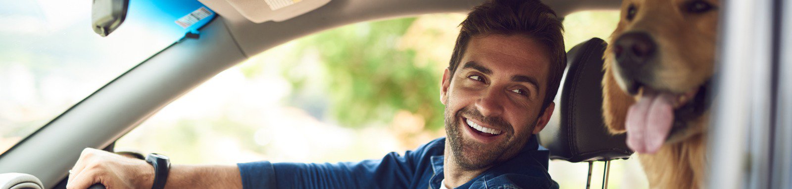 A man driving  a car and smiling at dog inside the car.