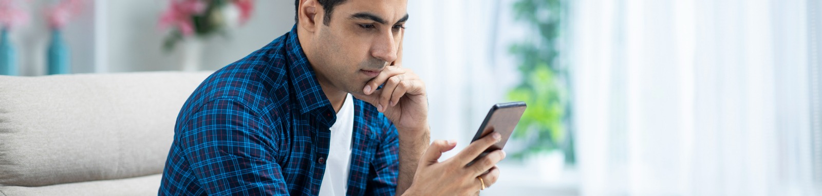Man looking at his phone at home with a serious expression