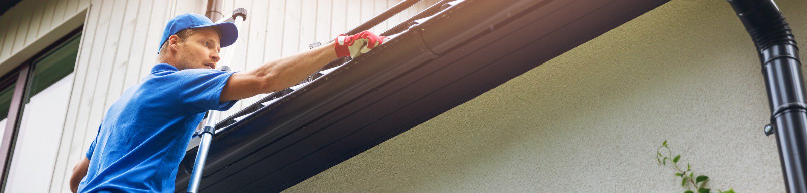 Man on ladder cleaning house gutter