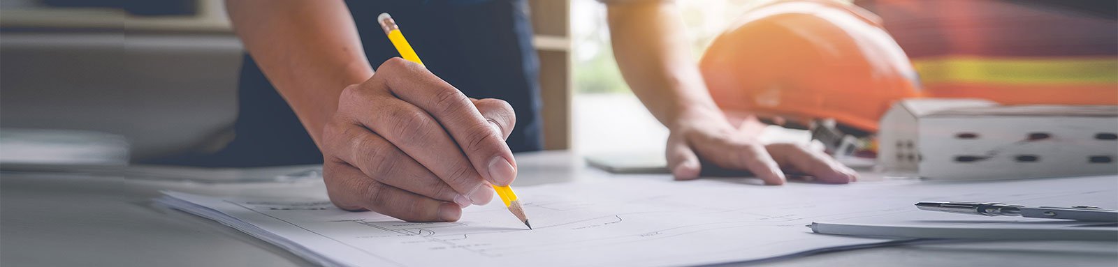 Man with hardhat drawing on building plans