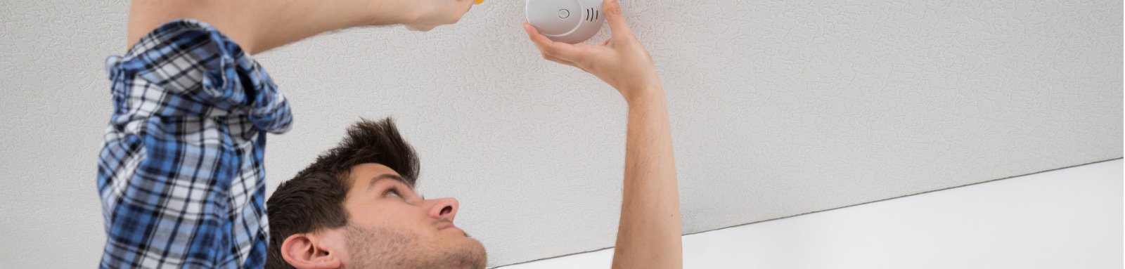 Man with screwdriver checking smoke detector