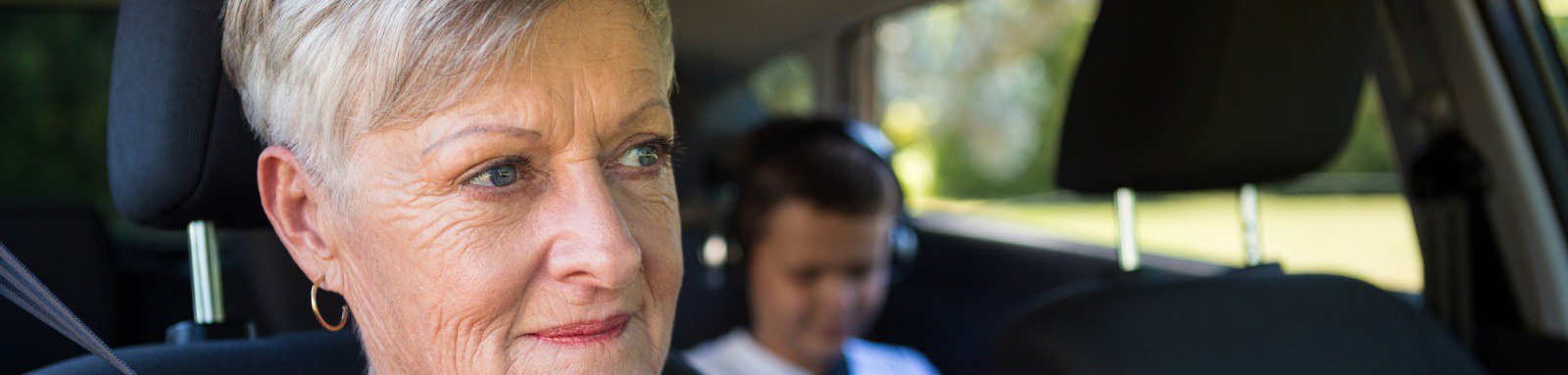 Mature woman driving looking ahead young boy backseat headphones in