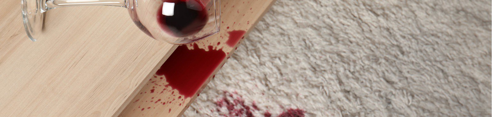 Overturned glass and spilled red wine on white carpet indoors