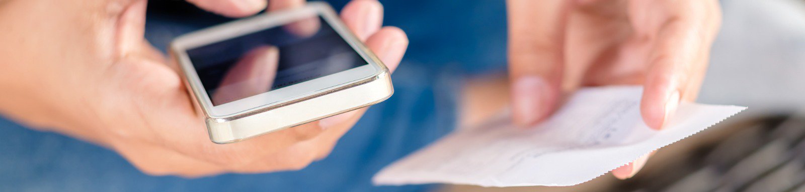 person holding smartphone in one hand and paper in the other