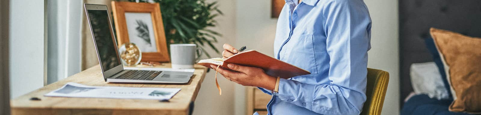 Person writing in notebook at desk with laptop