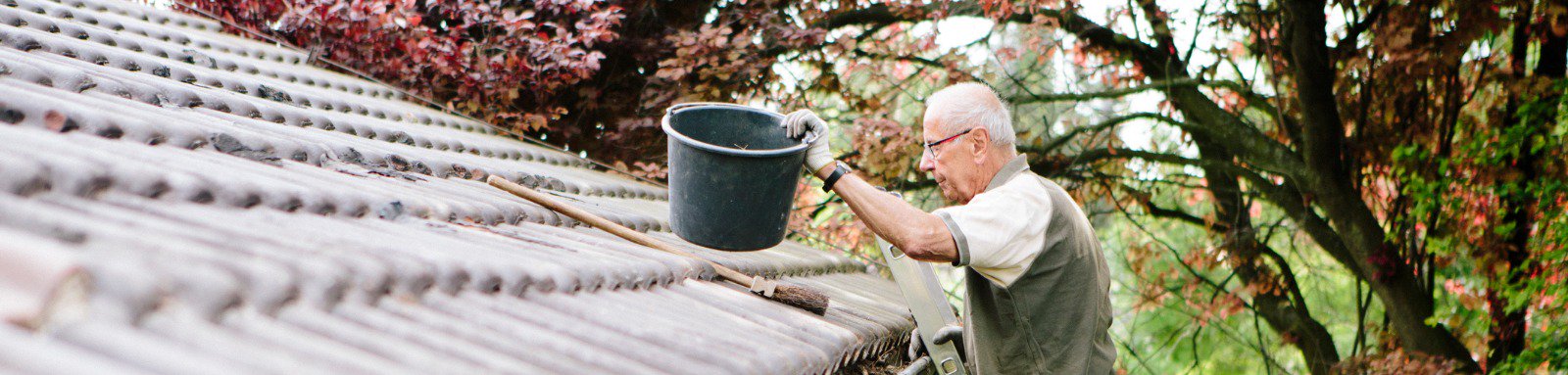 Senior man stands on ladder and cleans a roof gutter