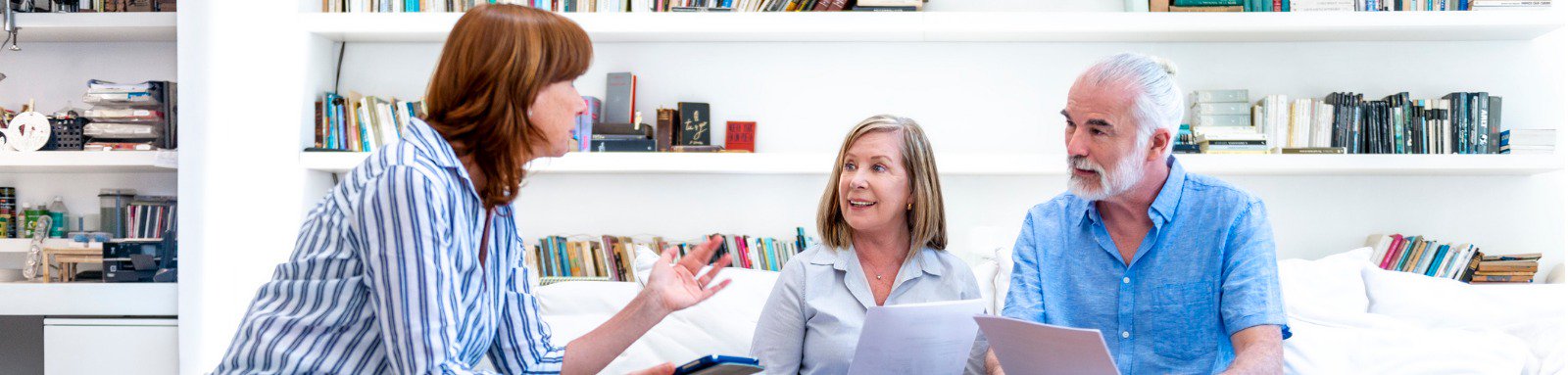 Two mature women and a man with documents talk on couch