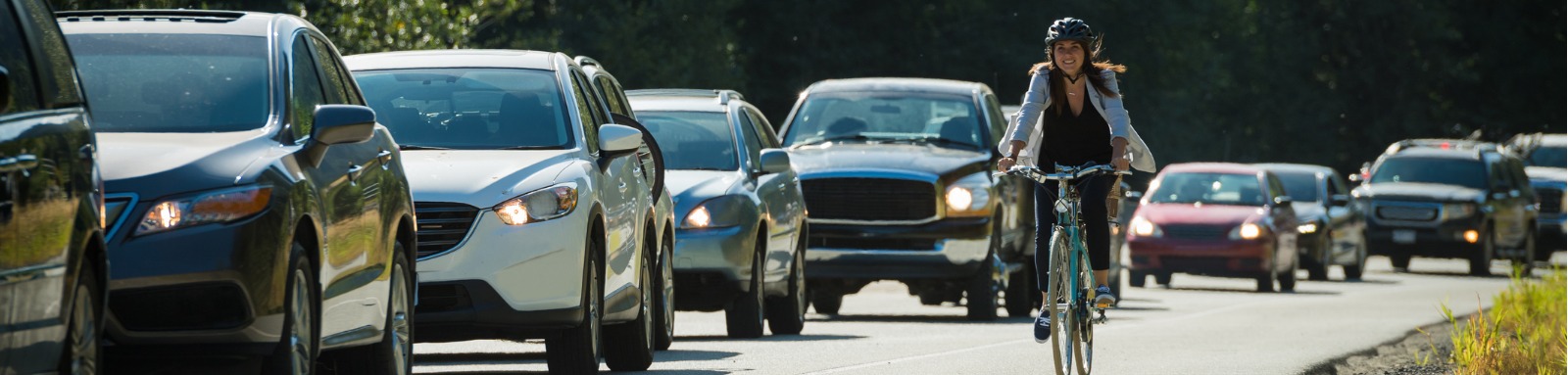 Woman riding bicycle past row of cars