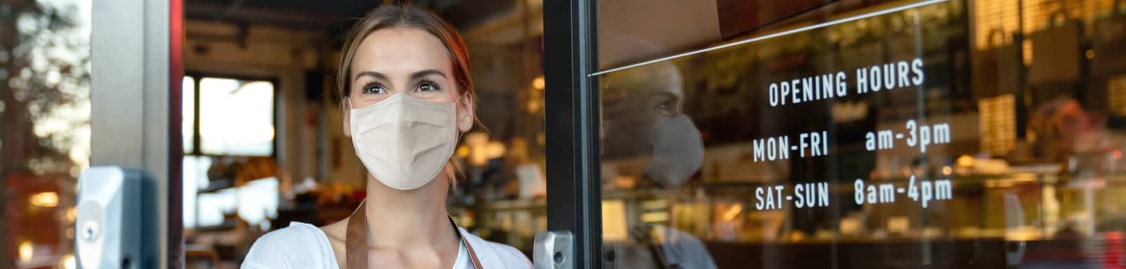 Woman wears mask in front of her cafe