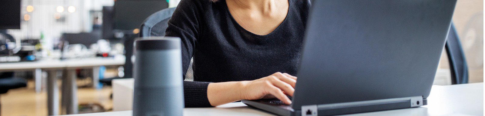 Woman using laptop on desk with voice activated speaker