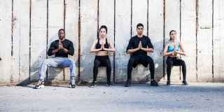 Four people sitting against wall outside